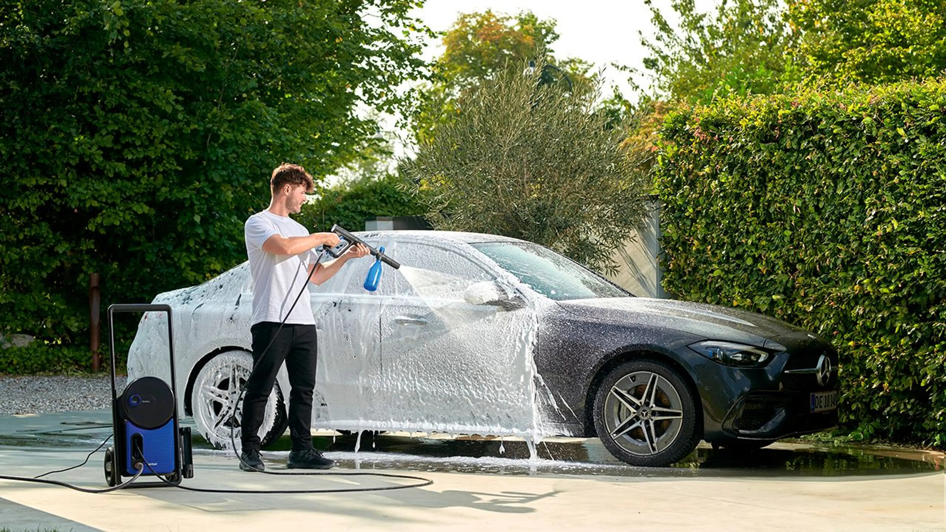 Mann som vasker bilen med høytrykkspyler og skumsprayer.