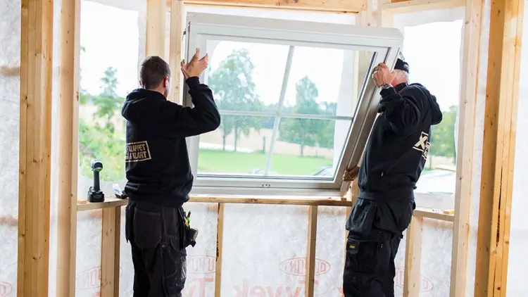 To håndverkere fra XL-BYGG setter inn et vindu i et nybygg.