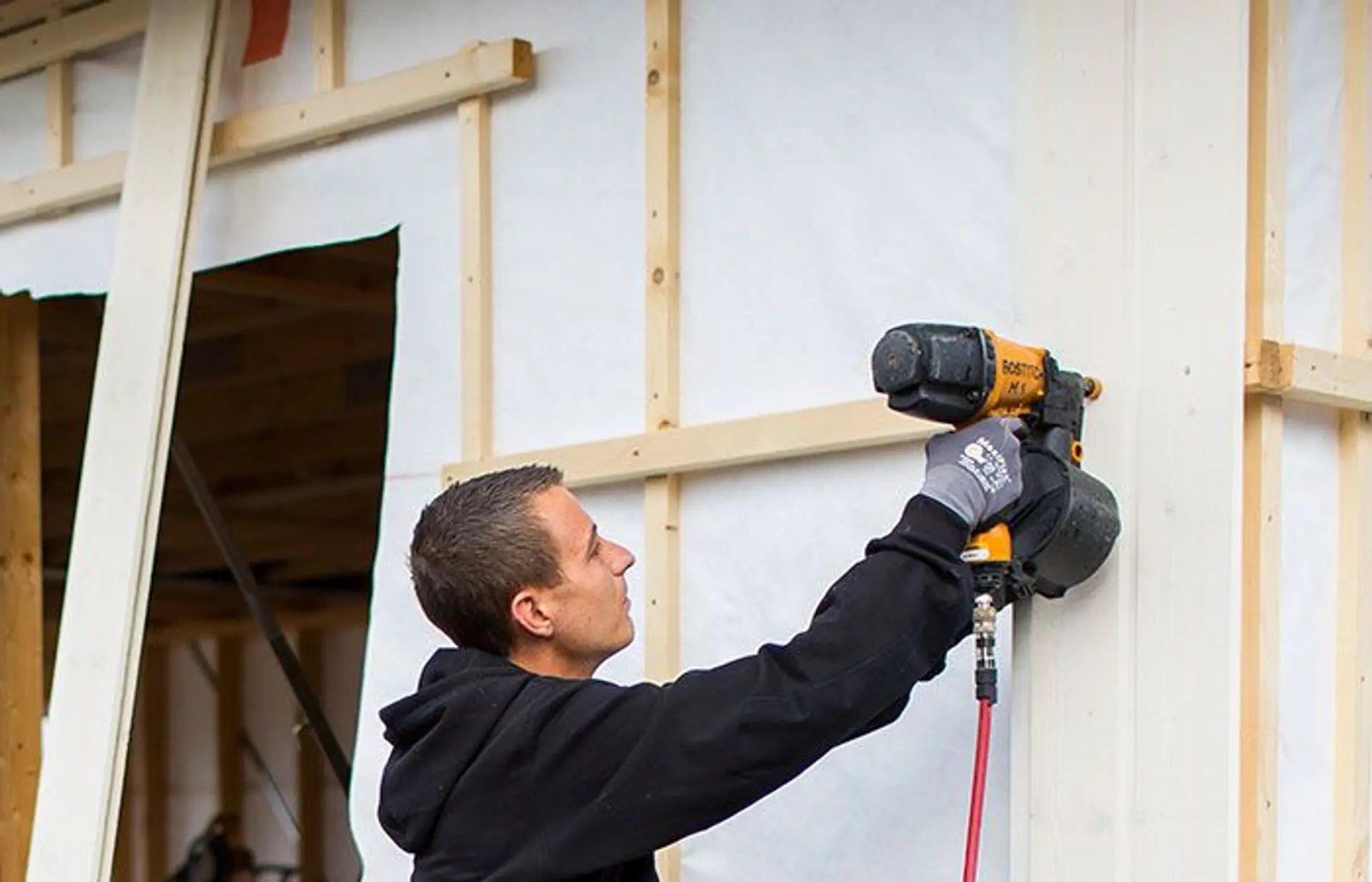 en mann monterer vindsperre på et hus uten kledning