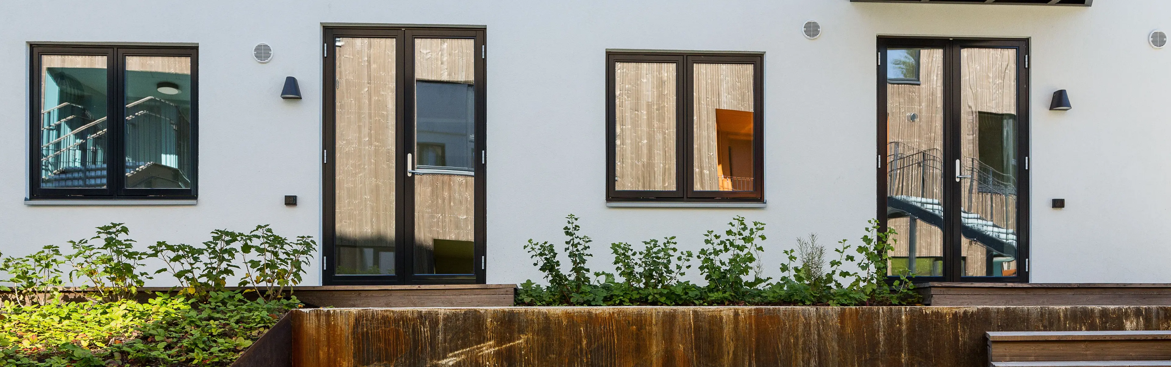 husfasade med to vinduer og to doble terrassedører i glass