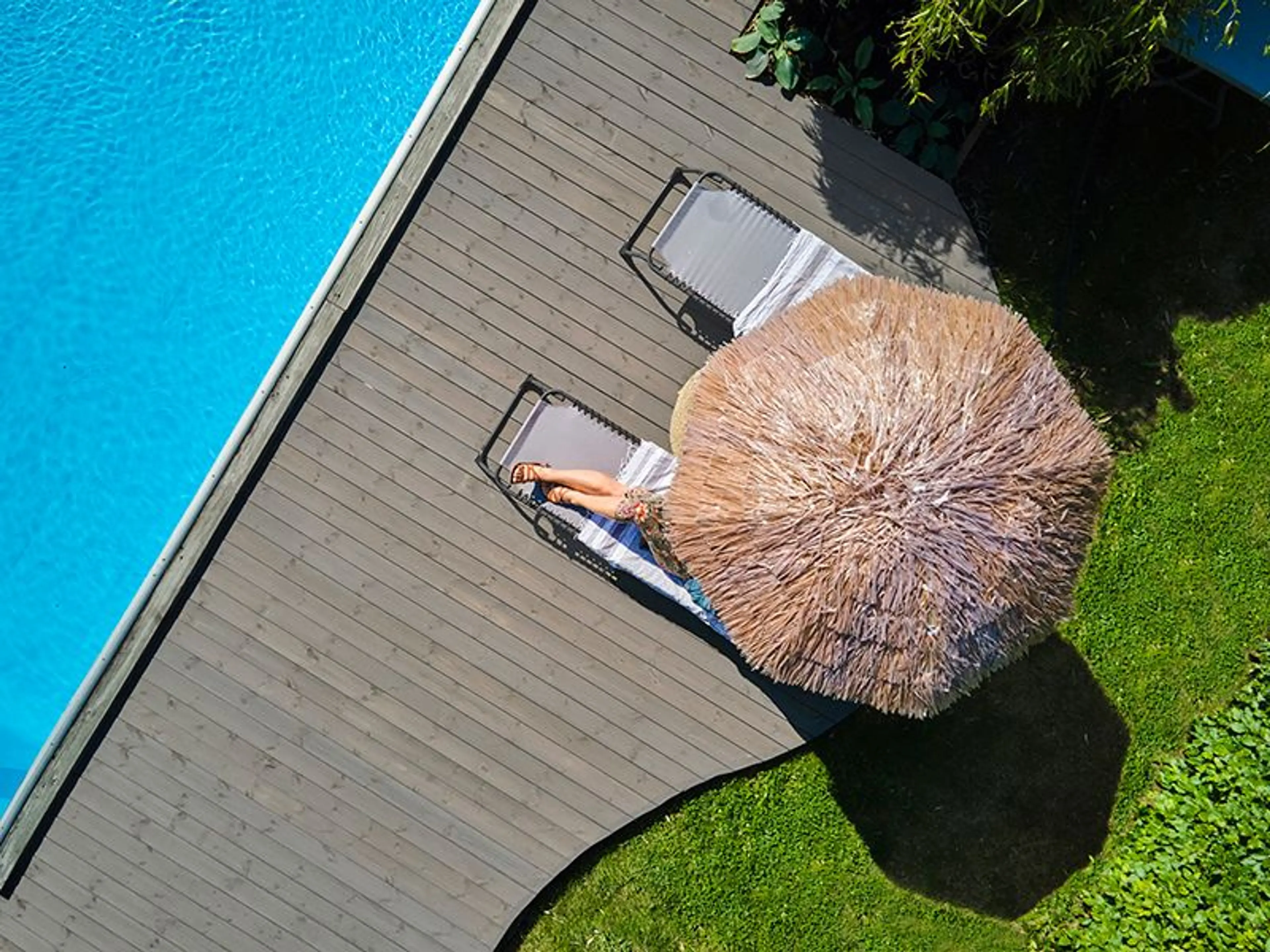 kvinne ligger på en solseng under en parasoll ved et basseng