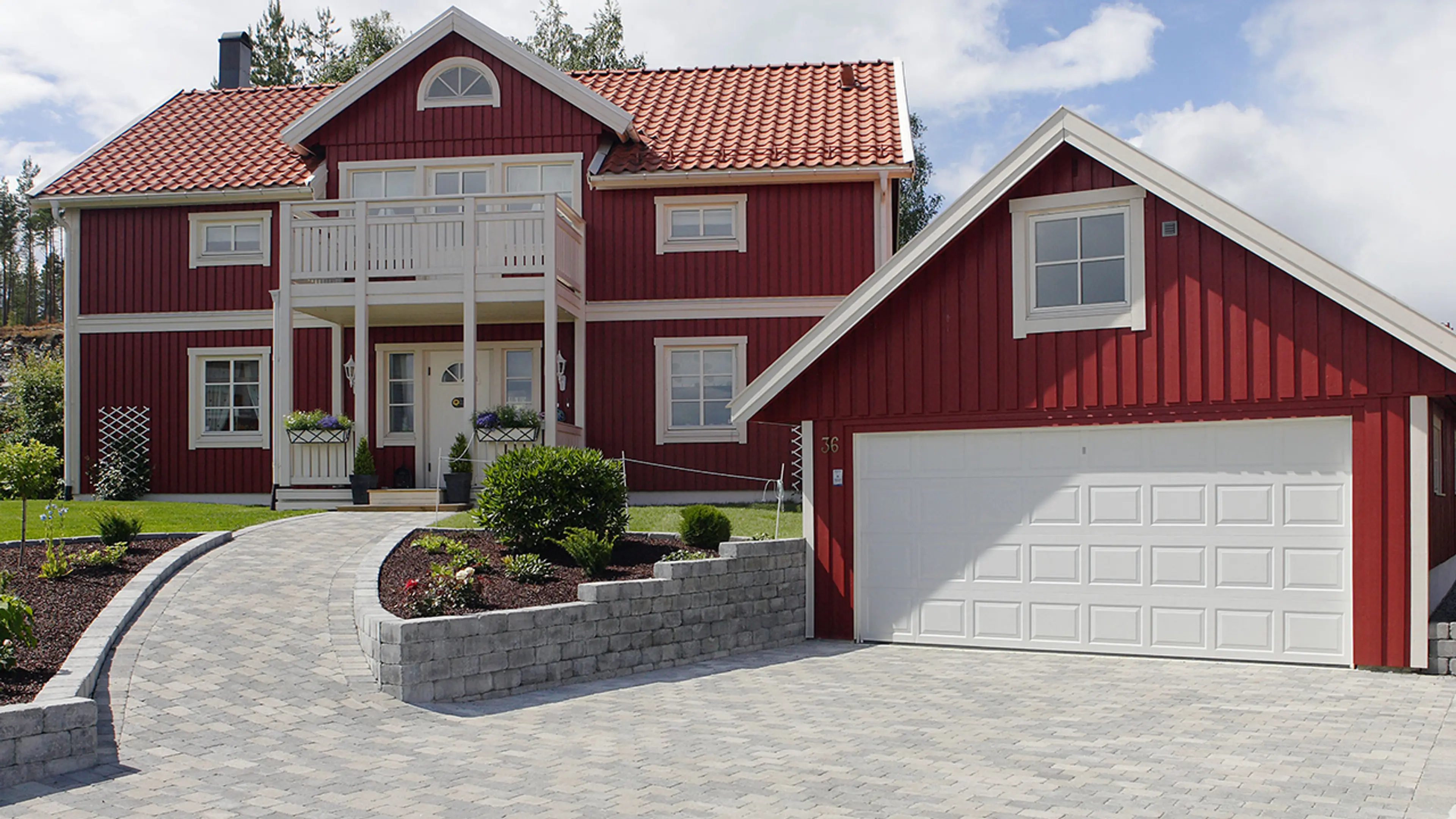 Rødt hus og garasje med belegningsstein i innkjørselen.