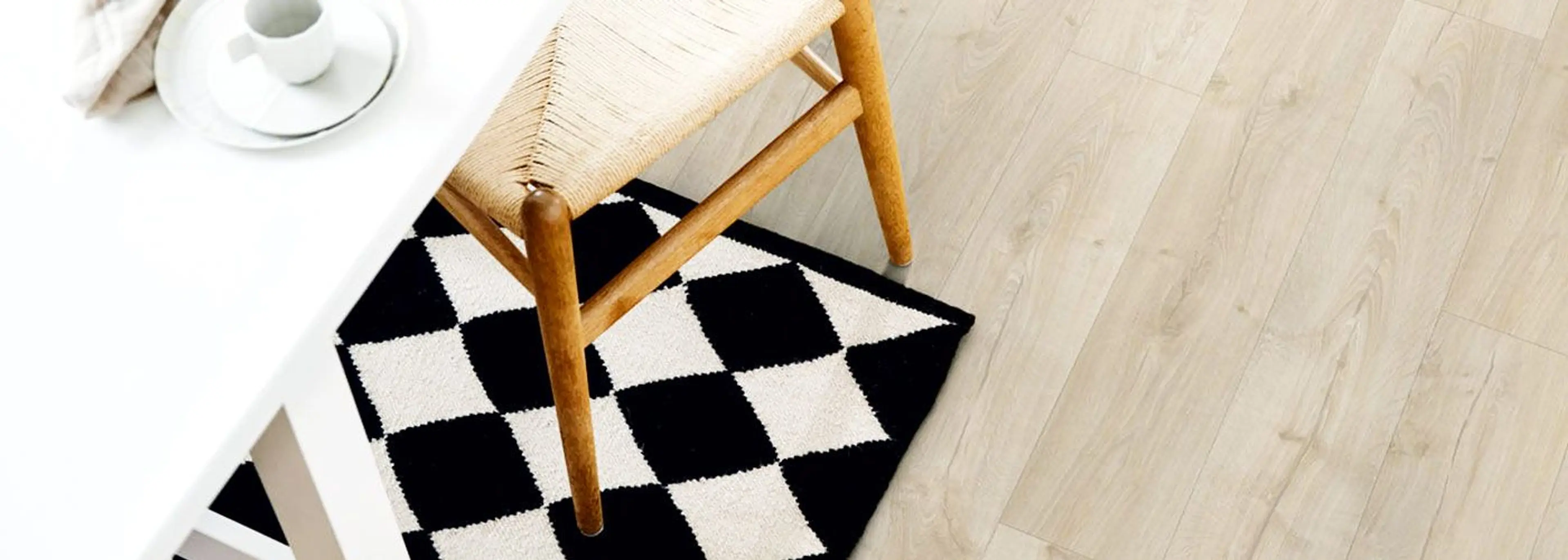 Lyst laminatgulv med sjakkrutet teppe, pinnestol og et hvitt spisebord