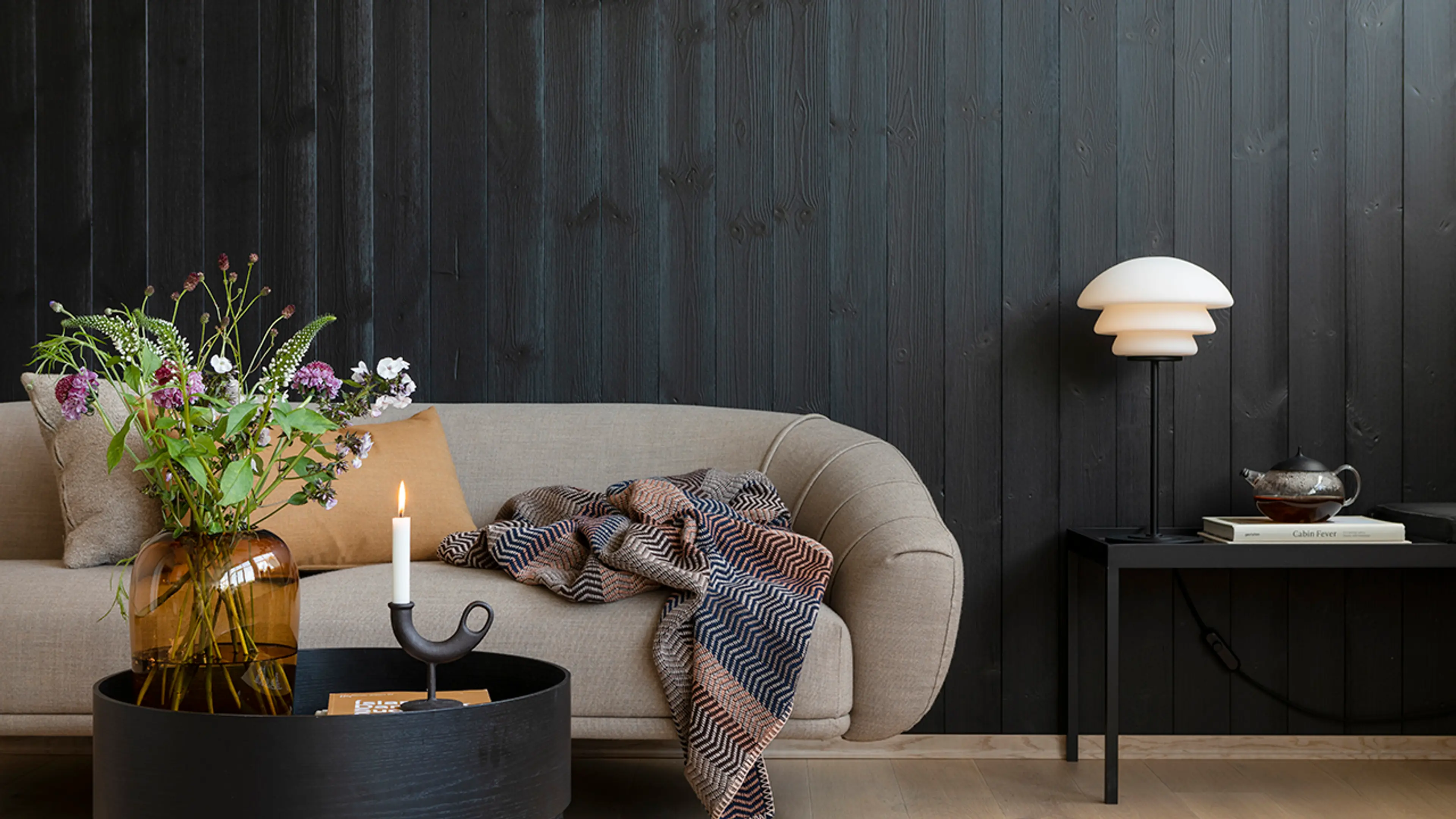 Moderne hytteinteriør hvor stue er i svart trepanel og har svarte møbler med stramme linjer.