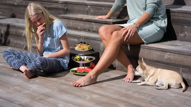 Jente, kvinne og hund sitter på en terrasse i varmebehandlet furu.