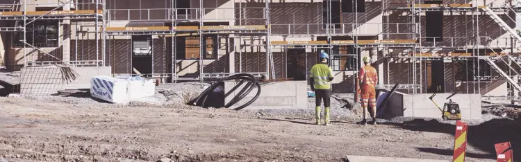 to menn står på en byggeplass og ser på et rekkehus som er under oppføring
