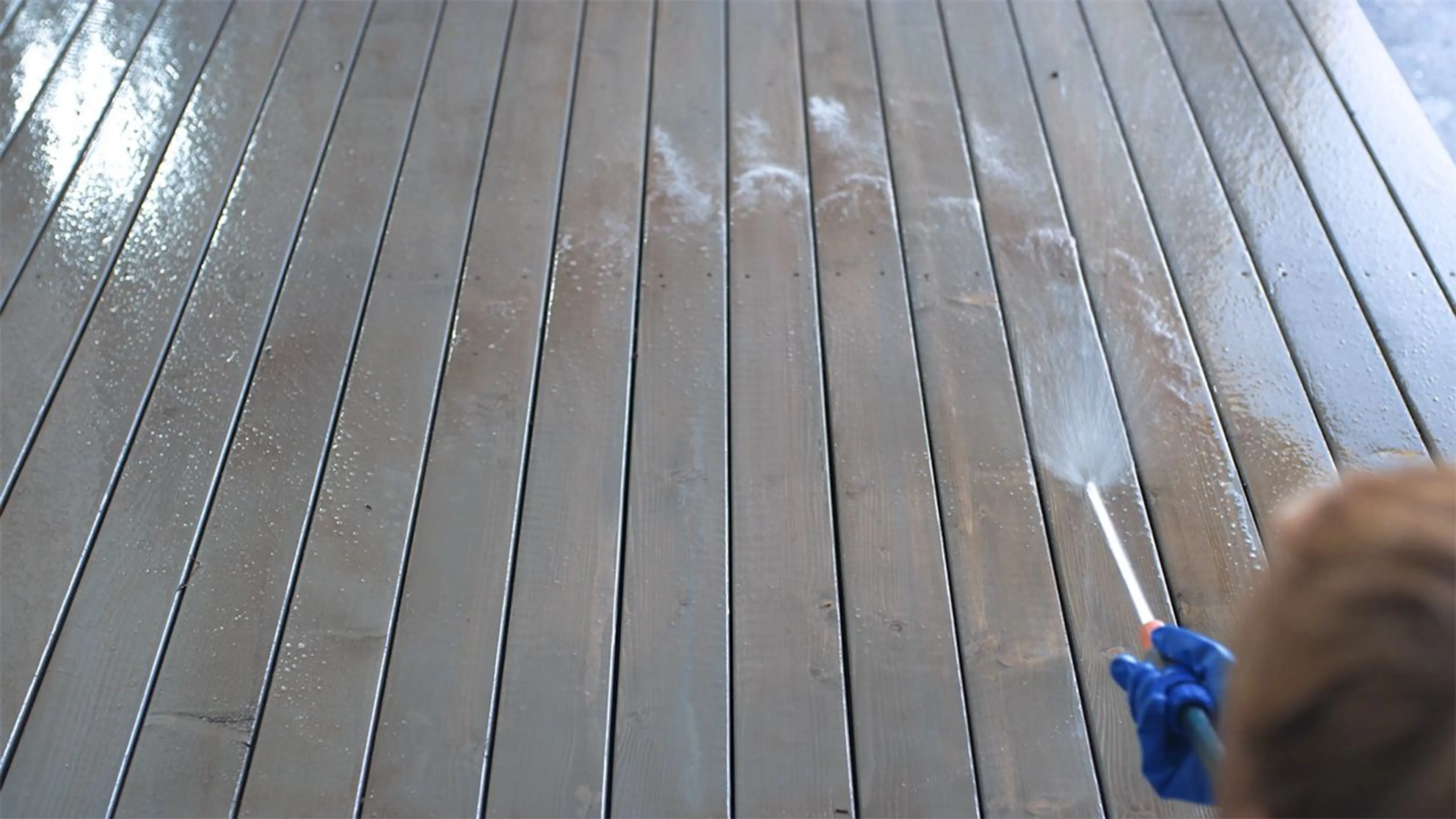 Person som spyler med hageslange for å vaske terrasse.
