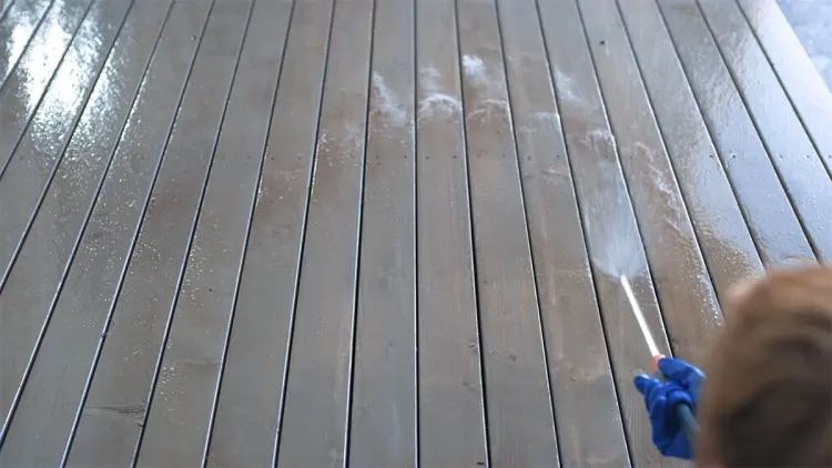 Person vasker terrassen med en hageslange.