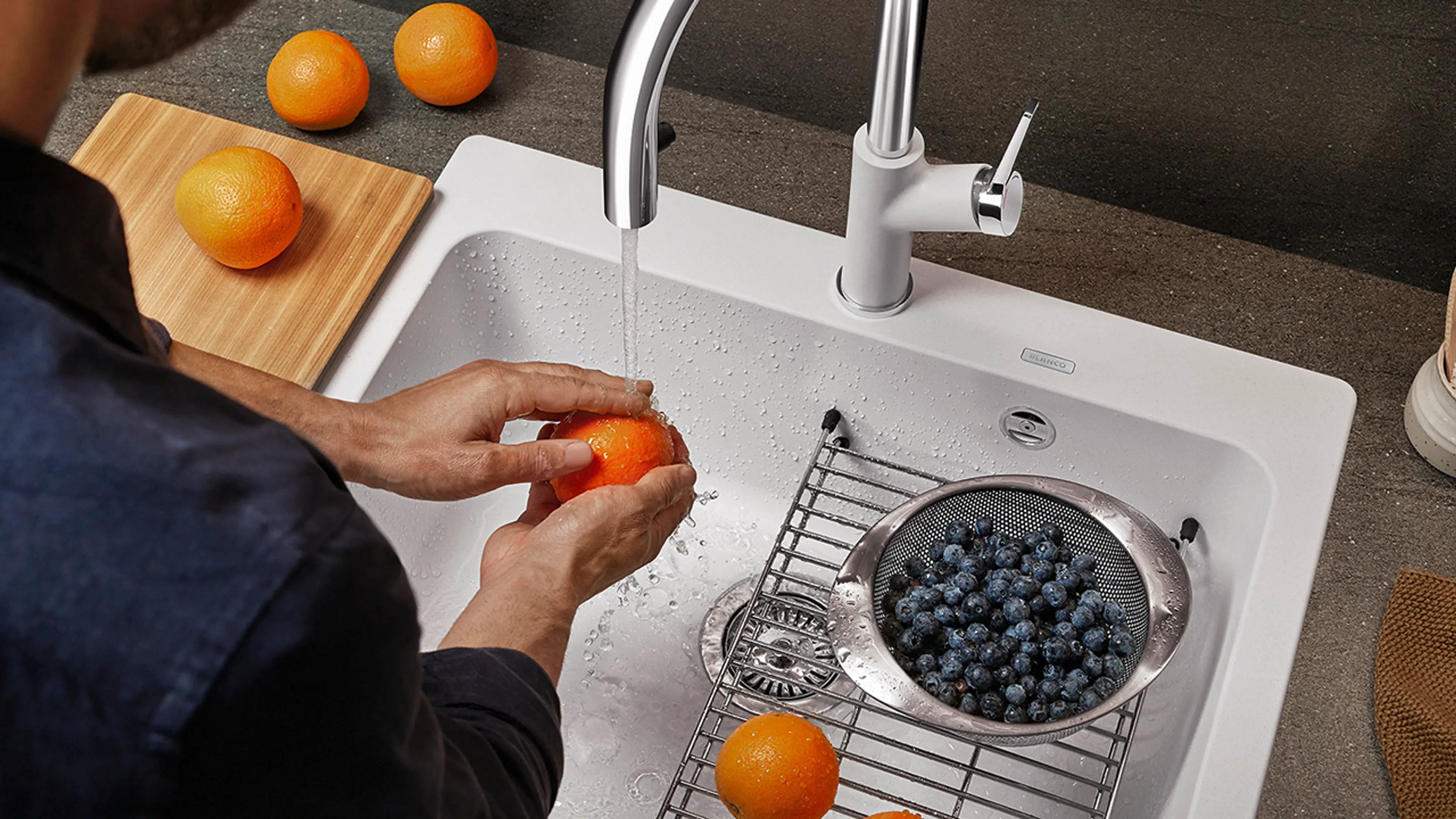 Mann som skyller appelsiner og blåbær i smart kjøkkenvask med rist til å sette boller og legge frukten på.