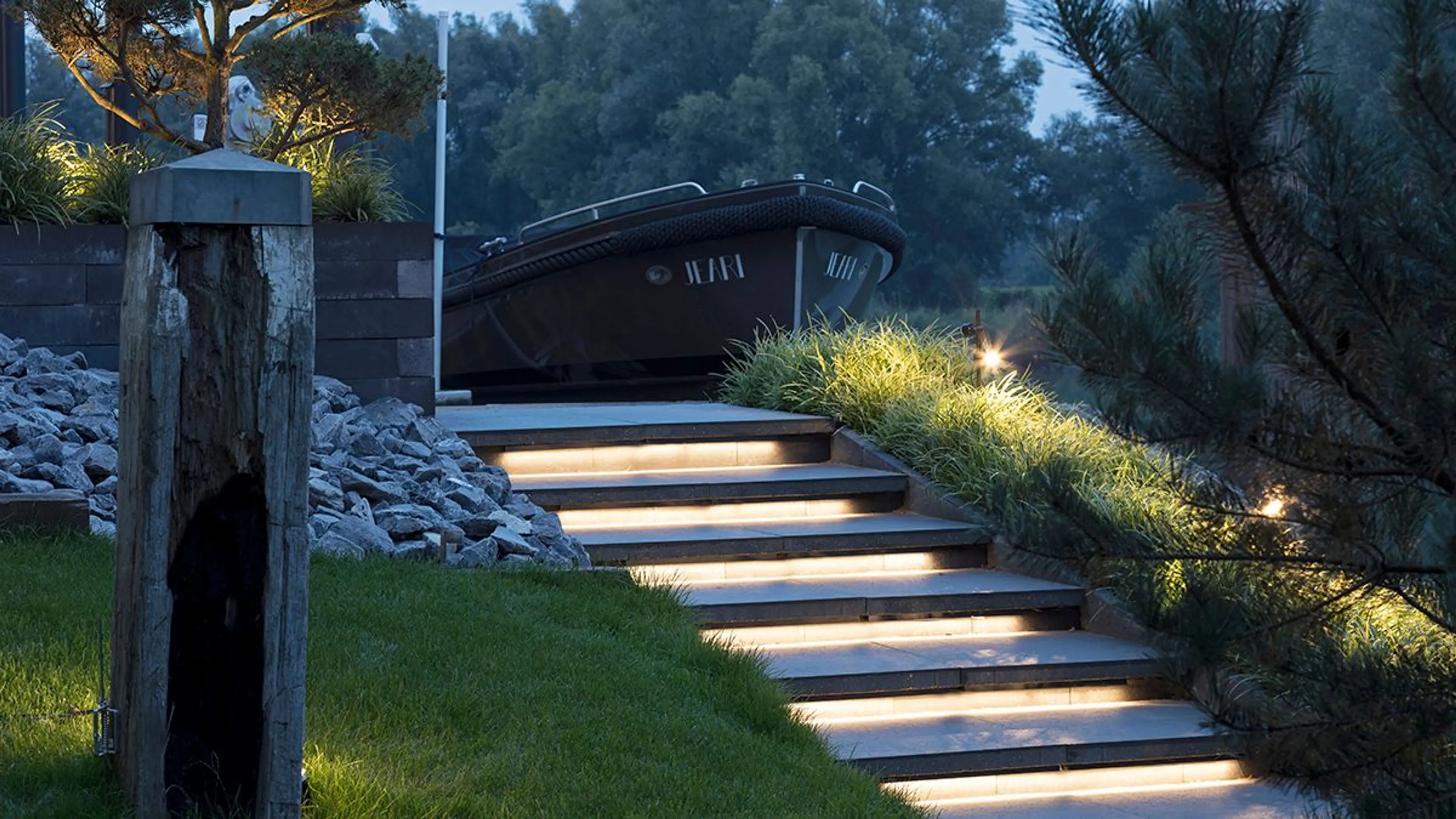 steintrapp i hage som er lyssatt og fører opp til en utstilt båt