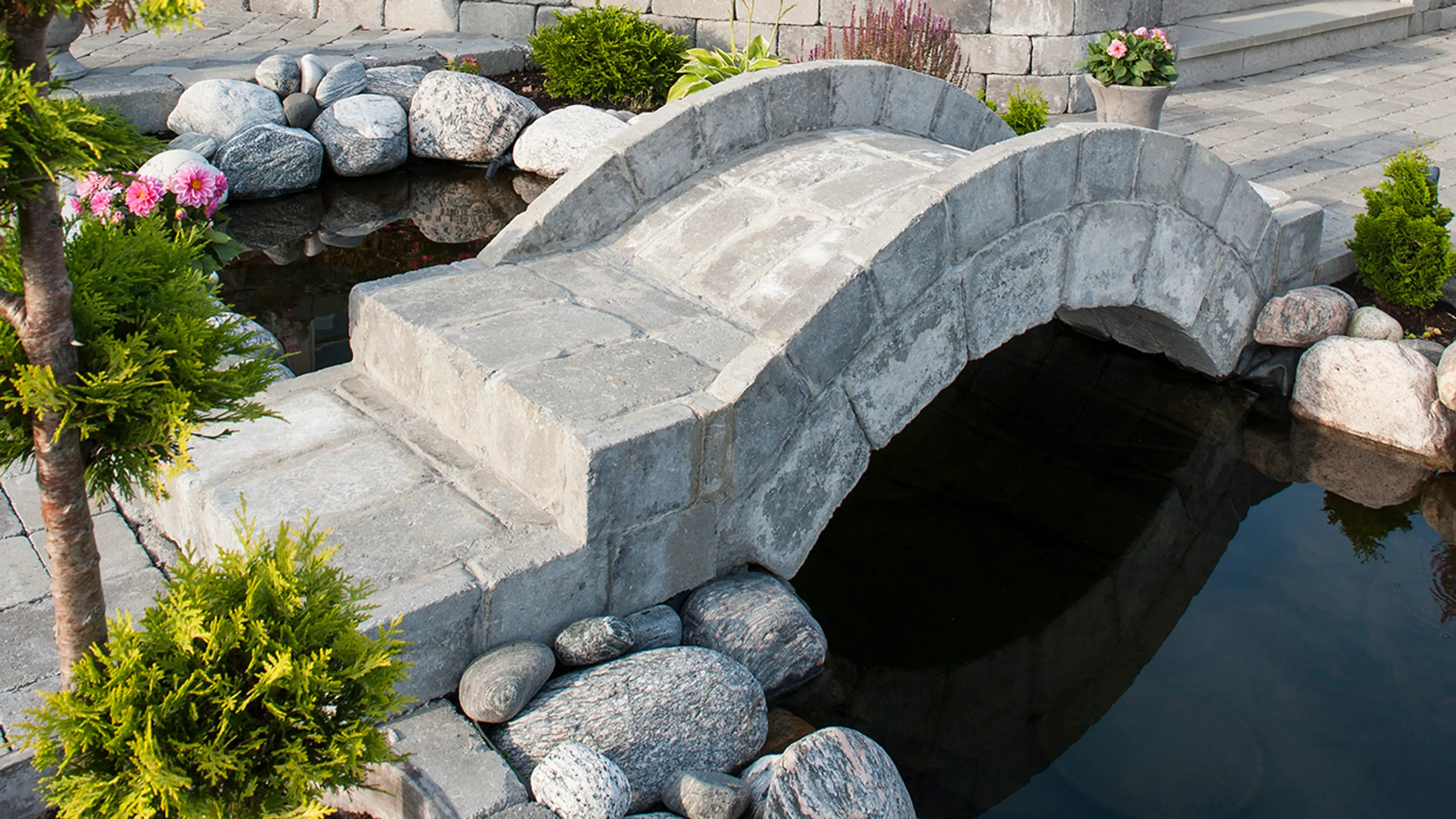 Store steiner til hagen som er lagt som dekorelement ved en dam med bro over.