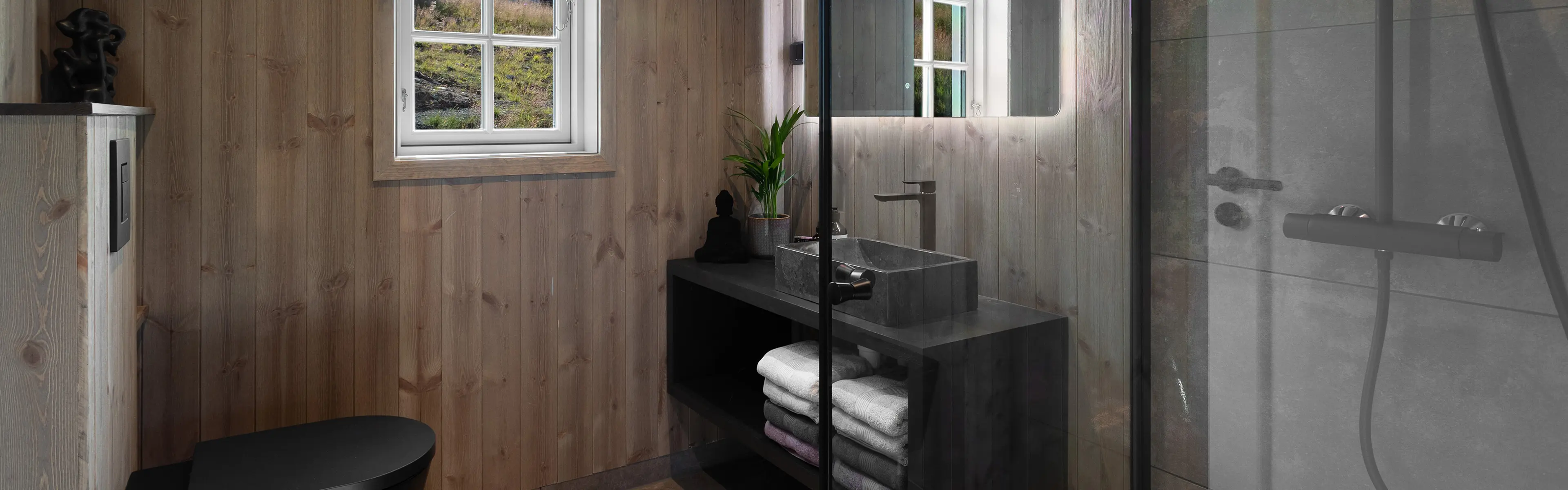 Hyttebad med sorte baderomsmøbler, sort vask og brunt trepanel på veggene.