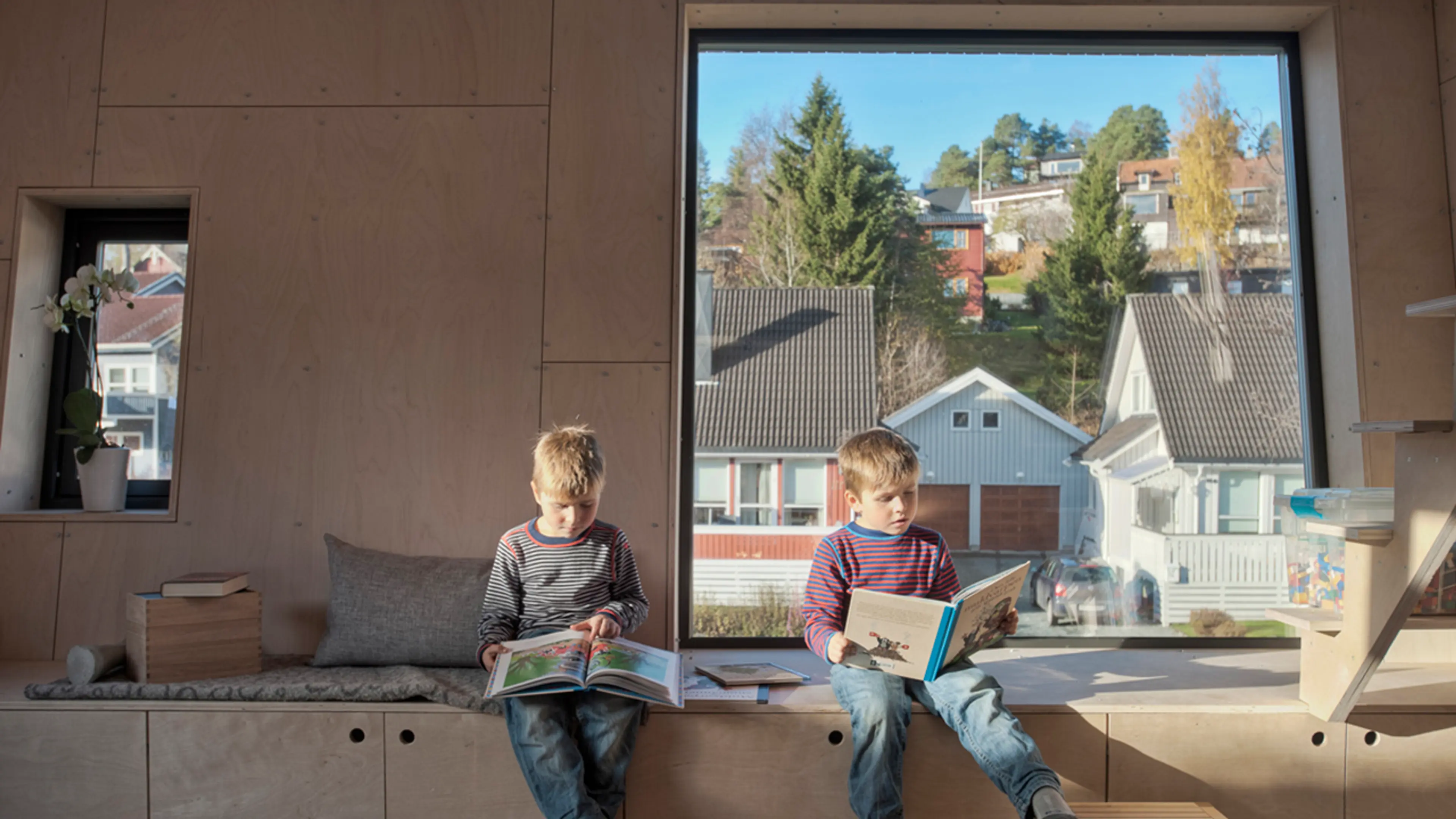To barn som leser bok foran et stort vindu.