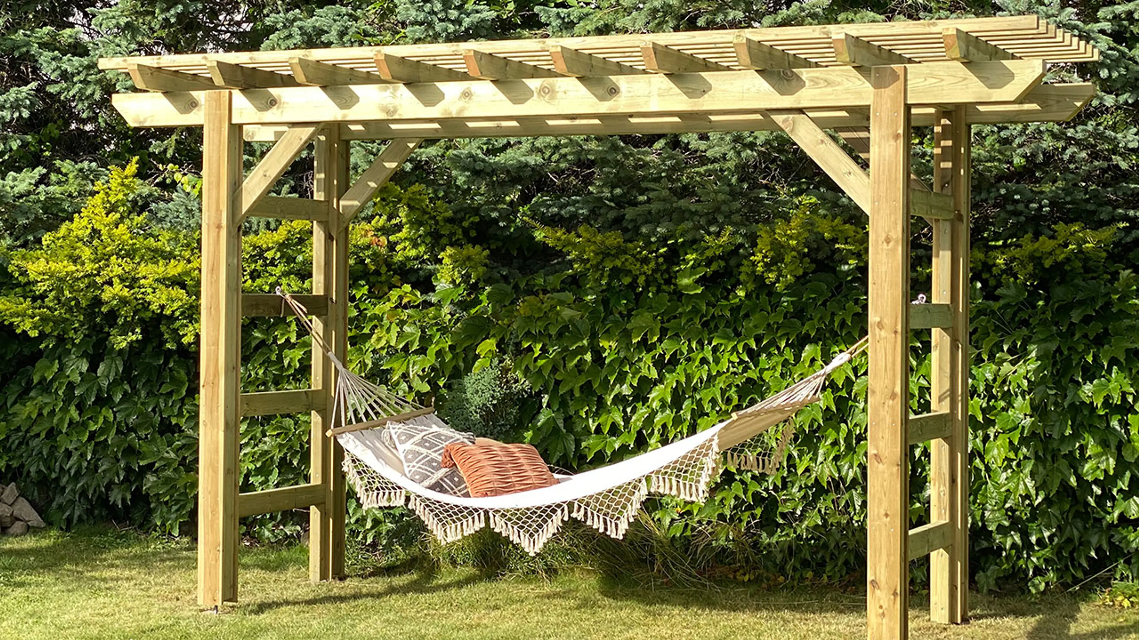 Grønn hage med liten frittstående pergola med hengekøye.
