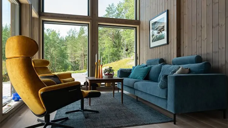 Innvendig panel i hytte med store vinduer og blå sofa.