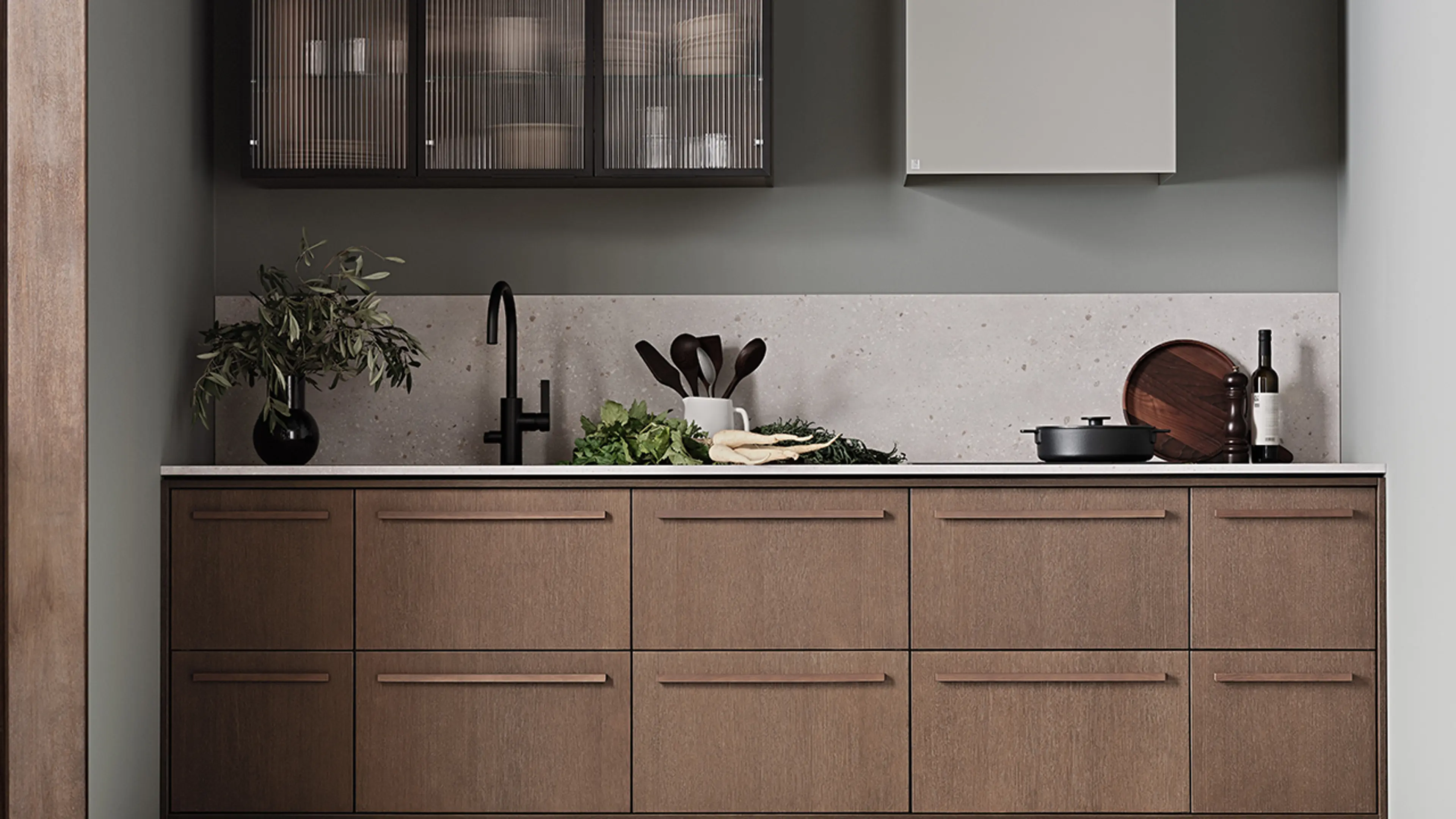 Lite kjøkken i treverk med kjøkkenhette og overskap med glassfronter.