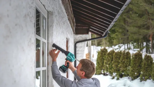 Mann som vedlikeholder vinduene på hvitt murhus.