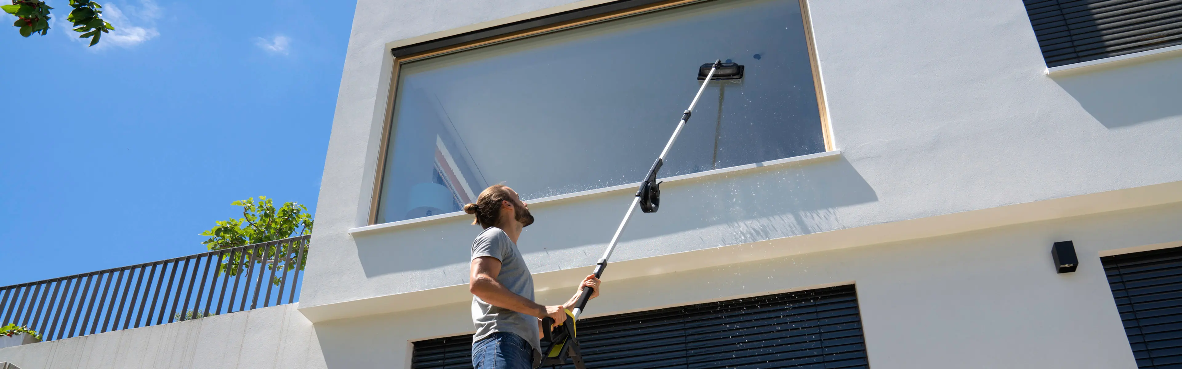 Mann som vasker vinduer ute med teleskoplanse og vindussett til høytrykkspyler.