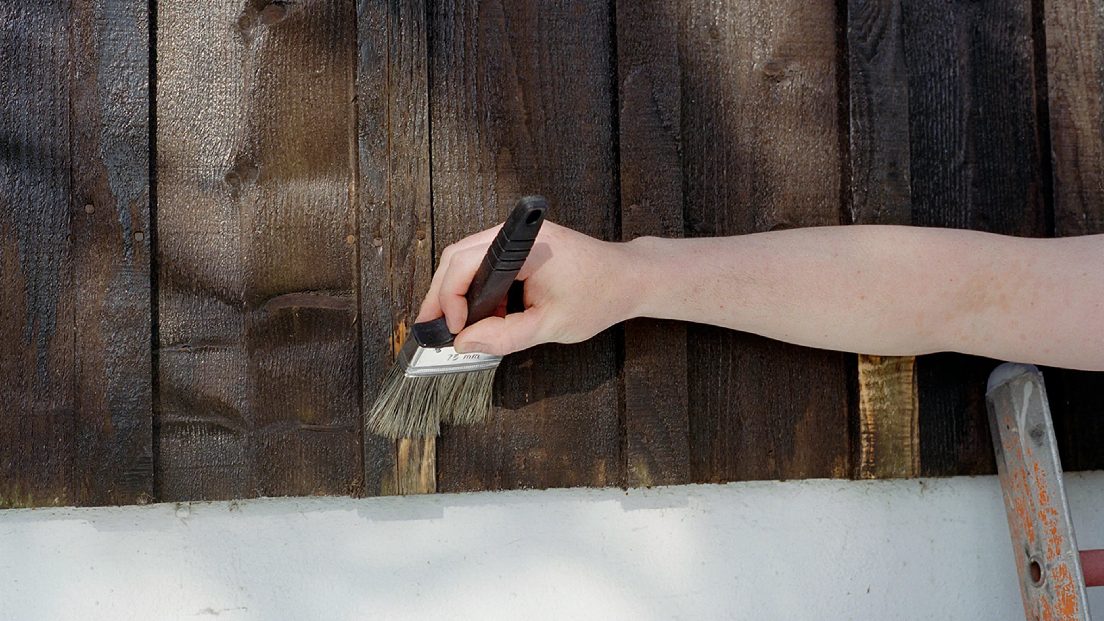 Nærbilde av hånd med pensel som skal male hus utvendig.
