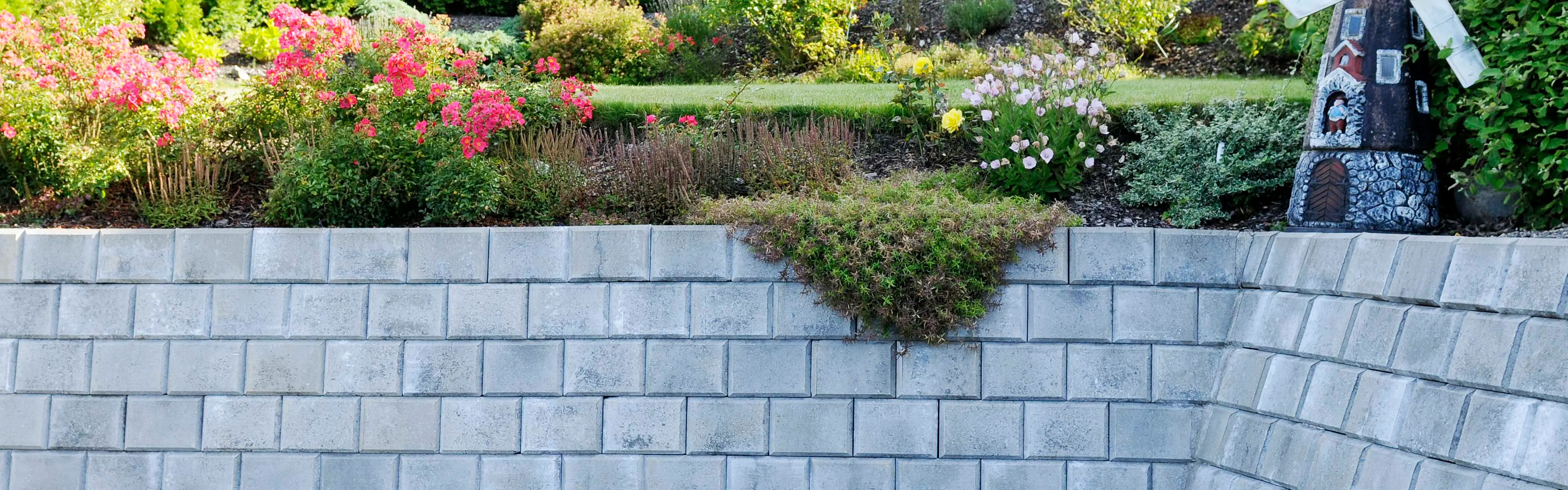 Støttemur i hage med blomsterbed og mini vindmølle.