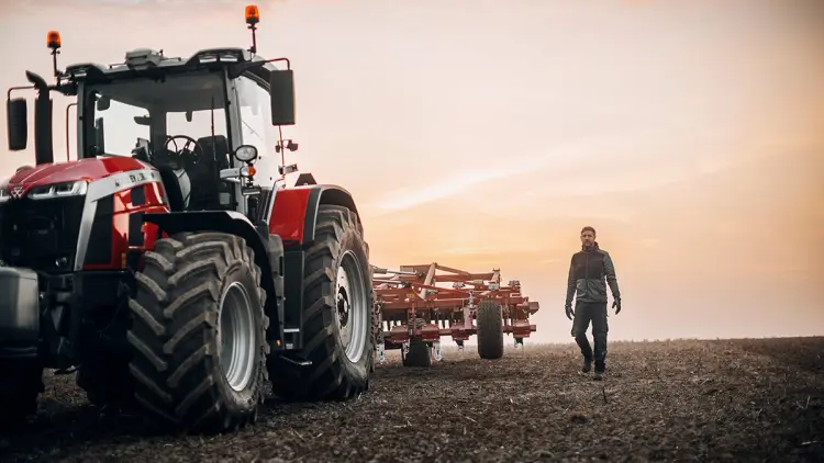 Mann som går i arbeidsklær med logo ved siden av en traktor på et jorde.