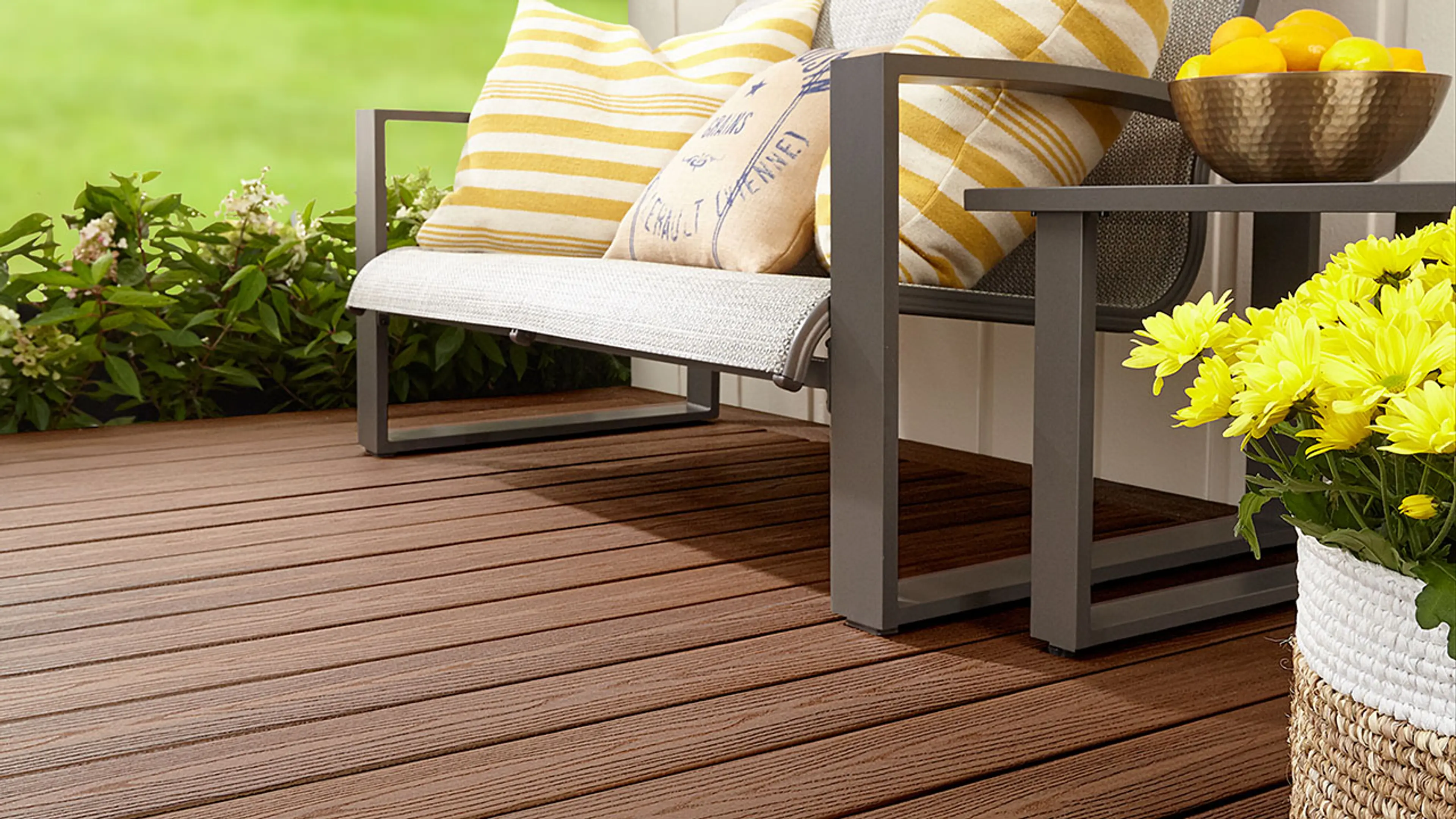 Flott terrasse med brune terrassebord, grønn hage og hagemøbler med gule detaljer.