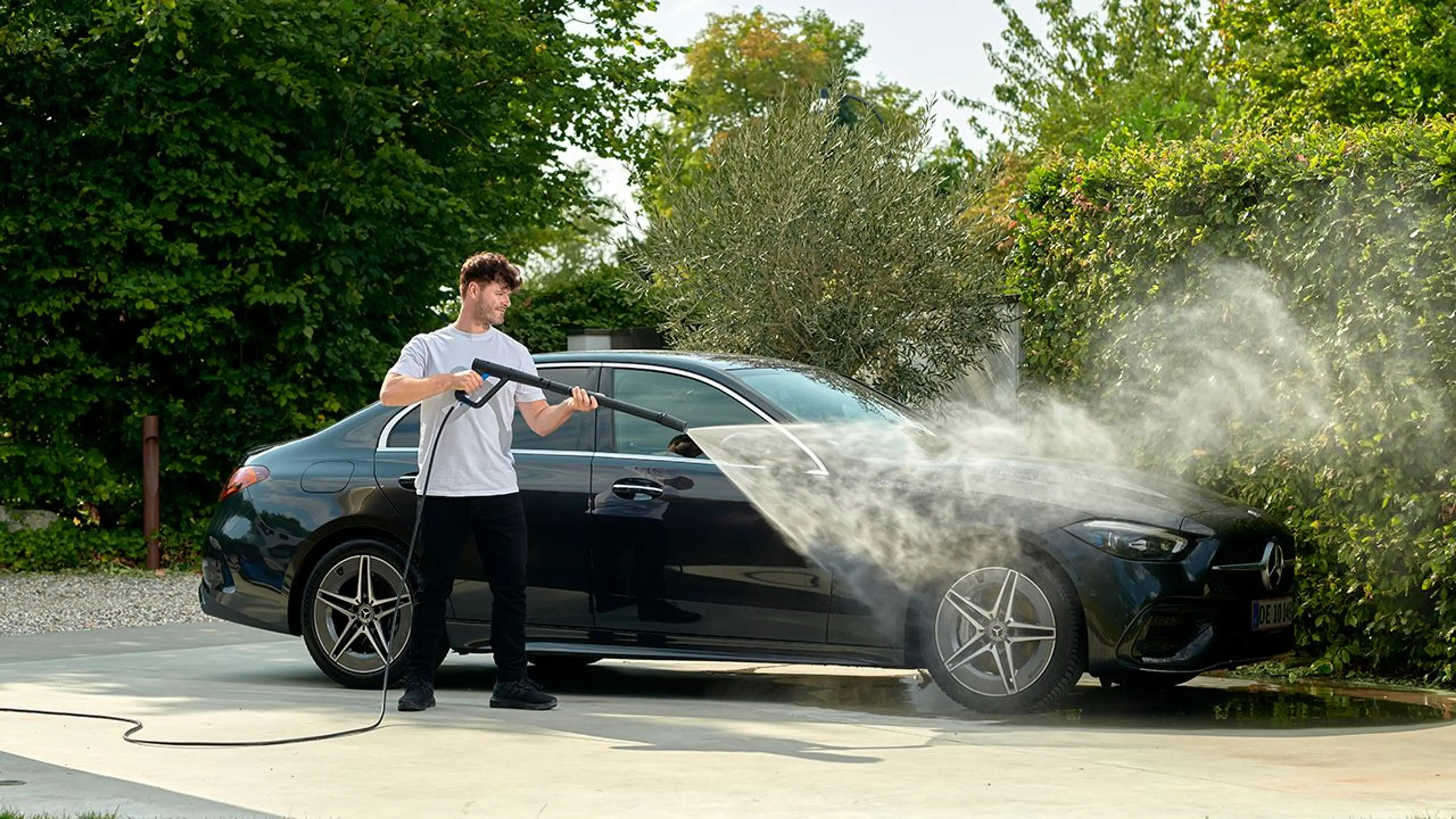Mann som spyler ren bilen med høytrykkspyler.