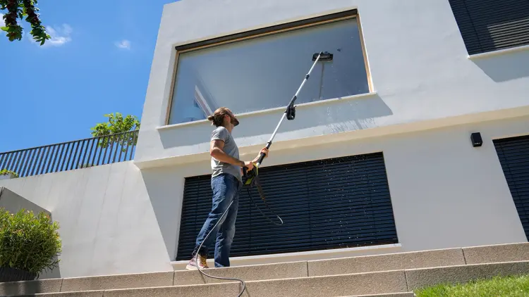 Mann som bruker teleskoplanse og vindussett til høytrykkspyler for å vaske vinduer ute.