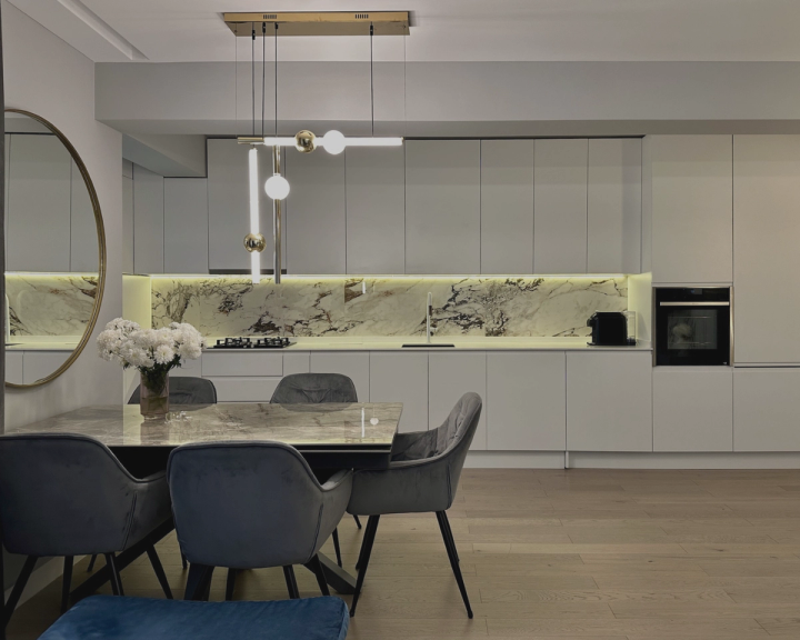 Bucătărie albă cu fronturi fără mânere, backsplash din marmură și masă cu scaune gri