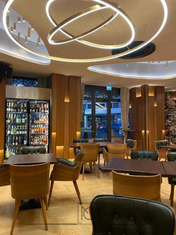 Restaurant cu lustră din inele luminoase, scaune din lemn și fotolii din piele verde