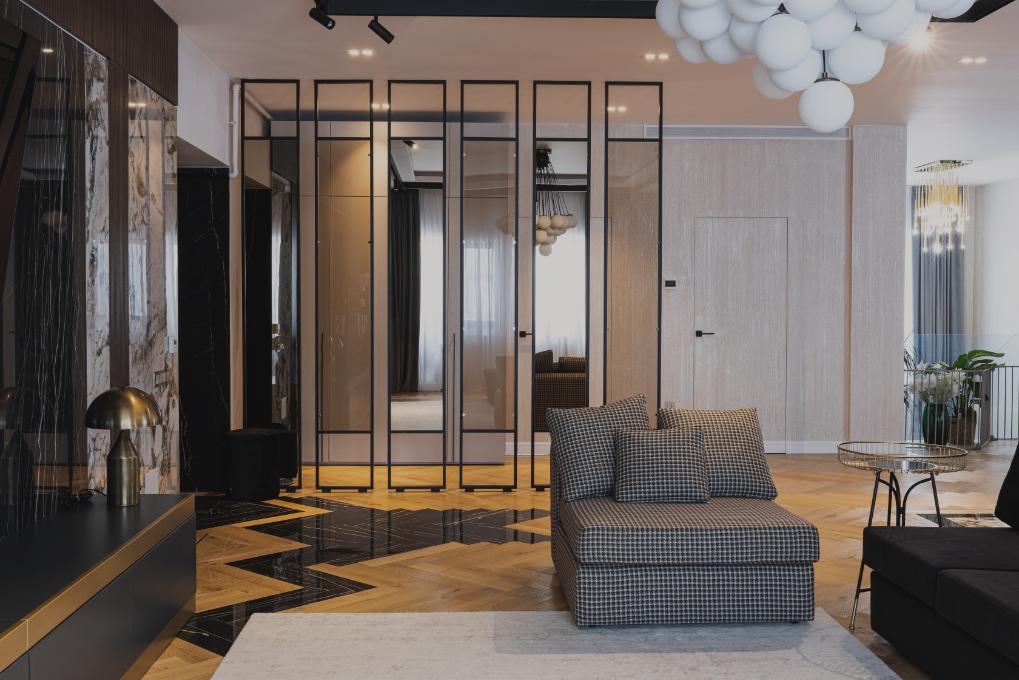 Living de penthouse cu parchet în spic, fotoliu în carouri și uși din sticlă cu profile negre
