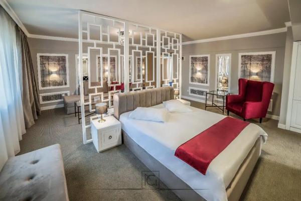 Cameră de hotel cu pat bej, banchetă și fotoliu roșu, în lumină naturală – Hotel Boavista, Timișoara