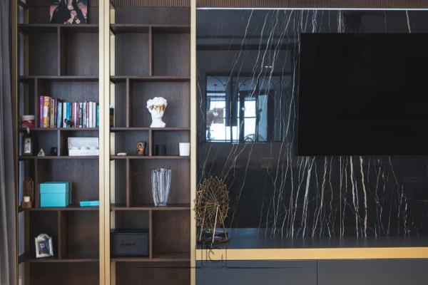 Detaliu de bibliotecă din lemn închis cu profile aurii lângă peretele TV din marmură neagră – Penthouse B. V., București