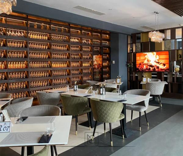 Restaurant cu perete de vinuri iluminat, scaune verzi matlasate și șemineu pe ecran – Elexus Poiana Brasov, Brașov