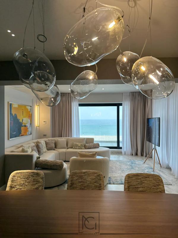 Living cu vedere la mare, canapea crem de colț și corpuri de iluminat din sticlă suflată