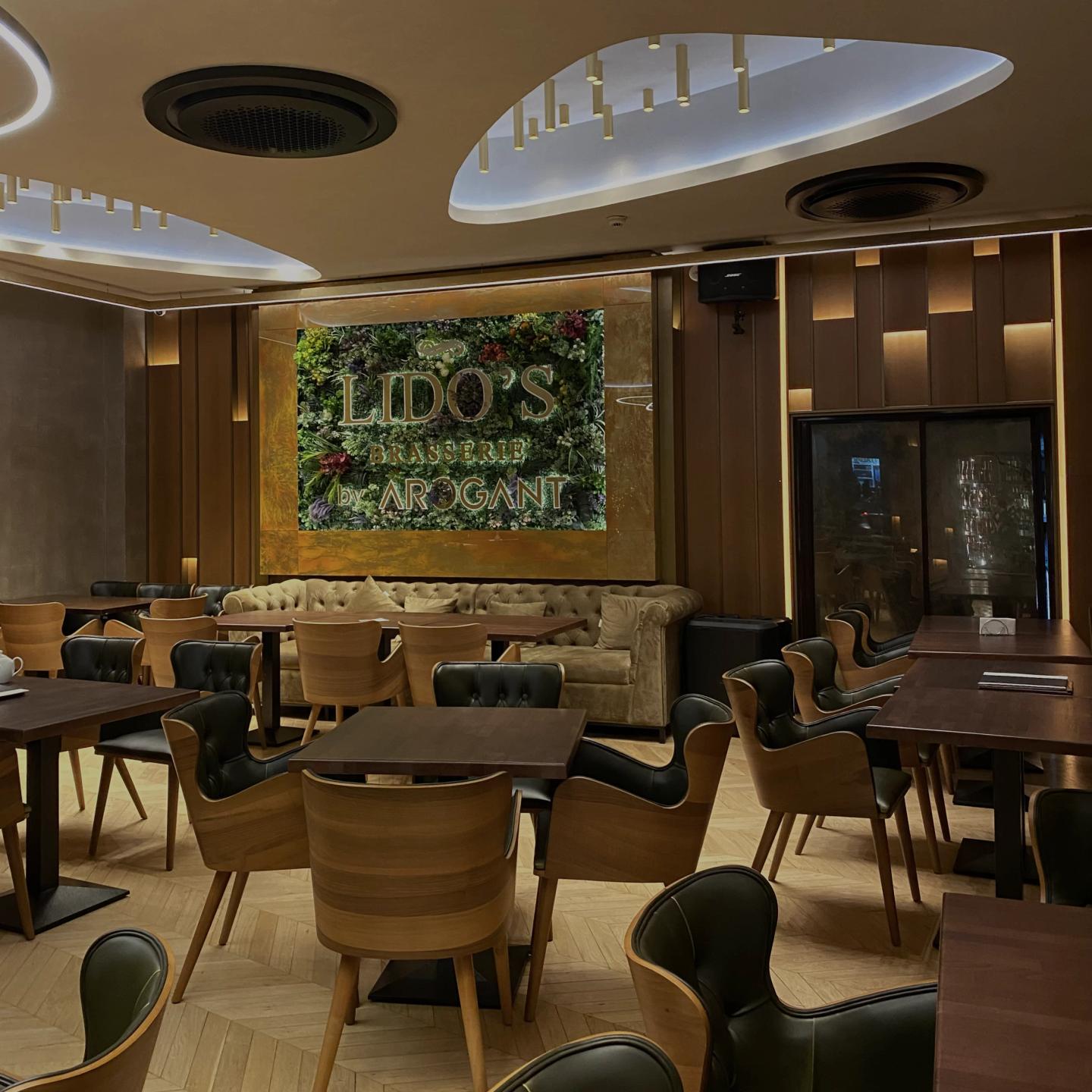 Salon Lido's Brasserie cu scaune din lemn curbat, perete verde cu logo și tavan cu iluminat