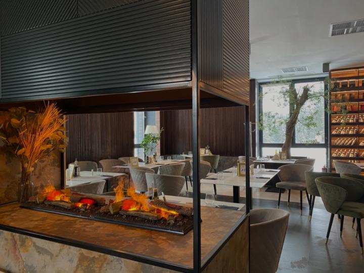 Restaurant cu șemineu încastrat într-o structură metalică neagră și scaune tapițate gri-verzi
