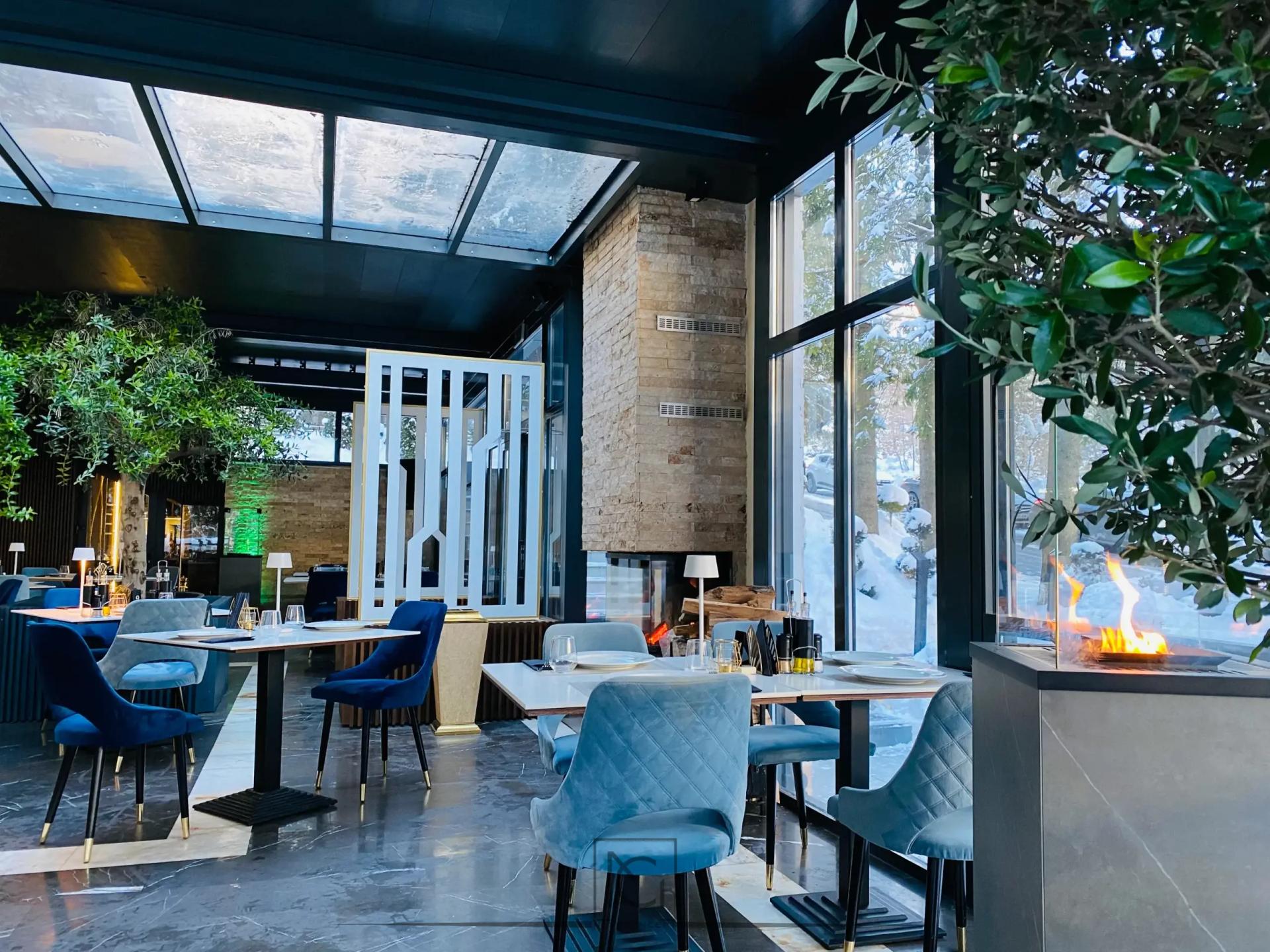 Salon de restaurant luminos cu mese pătrate, scaune albastre și paravan alb decorativ