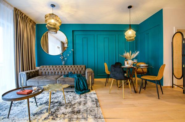 Living cu perete turcoaz, canapea gri capitonată, masă de dining și lustre aurii – Apartament Park View, București