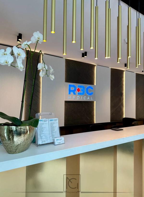 Detaliu de recepție cu orhidee albe, logo luminos și tuburi luminoase aurii – Romanian Bariatric Center, București