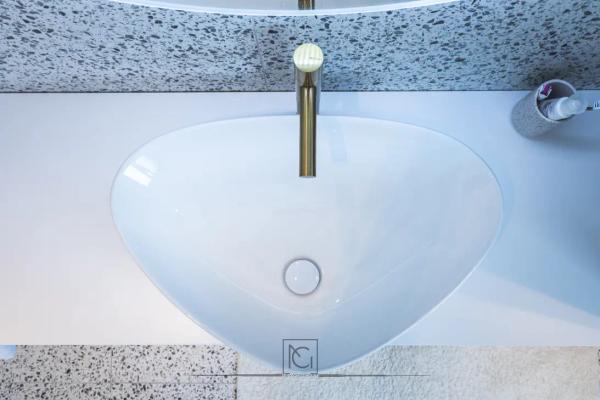 Detaliu de lavoar alb rotunjit cu baterie aurie pe blat terrazzo – Penthouse B. V., București