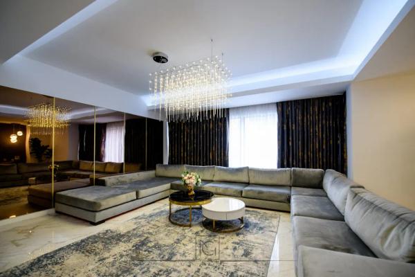 Living spațios cu canapea gri în formă de U, perete cu oglinzi bronz și lustră de cristal