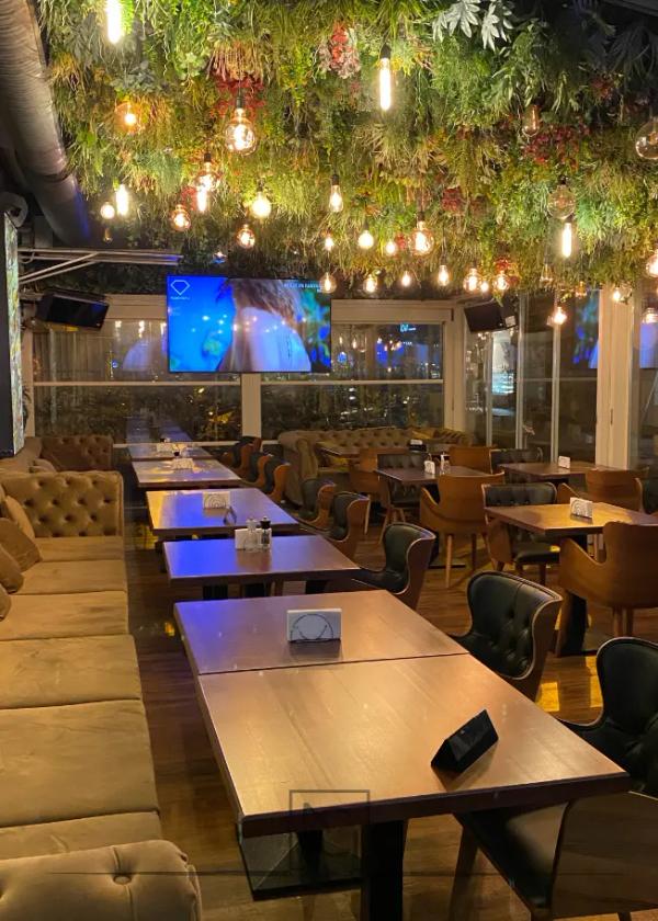 Terasă acoperită cu plante și ghirlande de becuri, banchete și mese din lemn – Lido's Brasserie by Arogant, București
