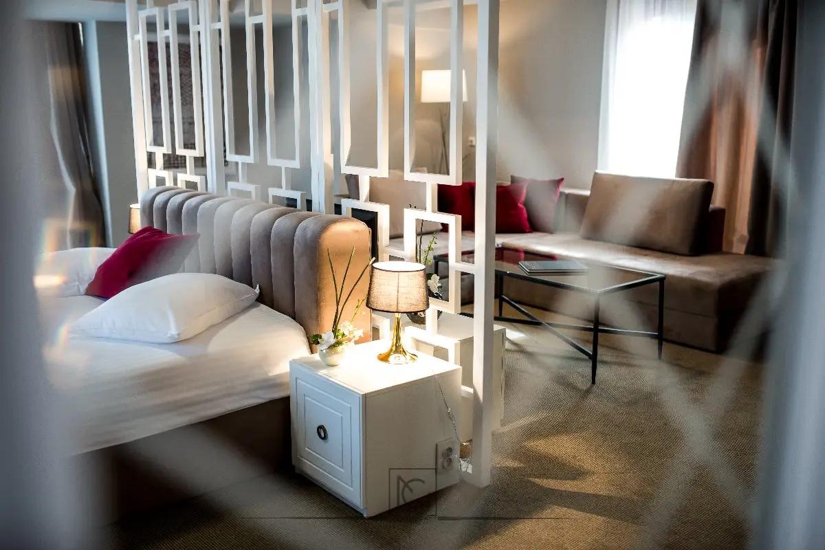 Pat de hotel cu noptieră albă și veioză aurie, lângă un paravan geometric alb – Hotel Boavista, Timișoara