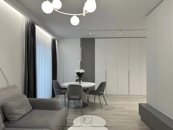 Zonă de dining cu masă rotundă albă, dulapuri albe pe un perete și lustră cu globuri