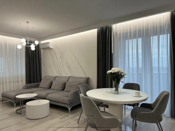 Living-dining cu canapea gri de colț, măsuțe albe rotunde și lustră cu globuri