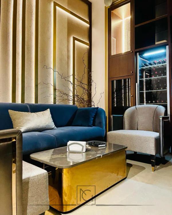Colț lounge cu canapea albastră, fotoliu gri și vitrină de băuturi iluminată
