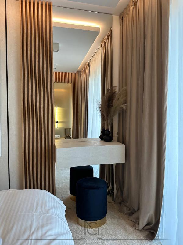 Colț de cameră de hotel cu masă de toaletă albă, taburet albastru și oglindă