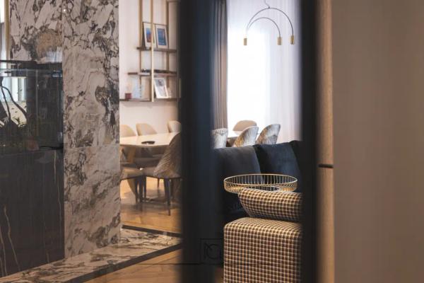 Vedere spre dining printre panouri de marmură, cu fotoliu în carouri în prim-plan – Penthouse B. V., București