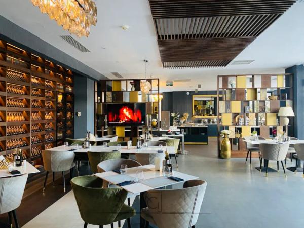 Salon de restaurant cu vitrină de vinuri pe perete, tavan cu lamele din lemn și scaune verzi